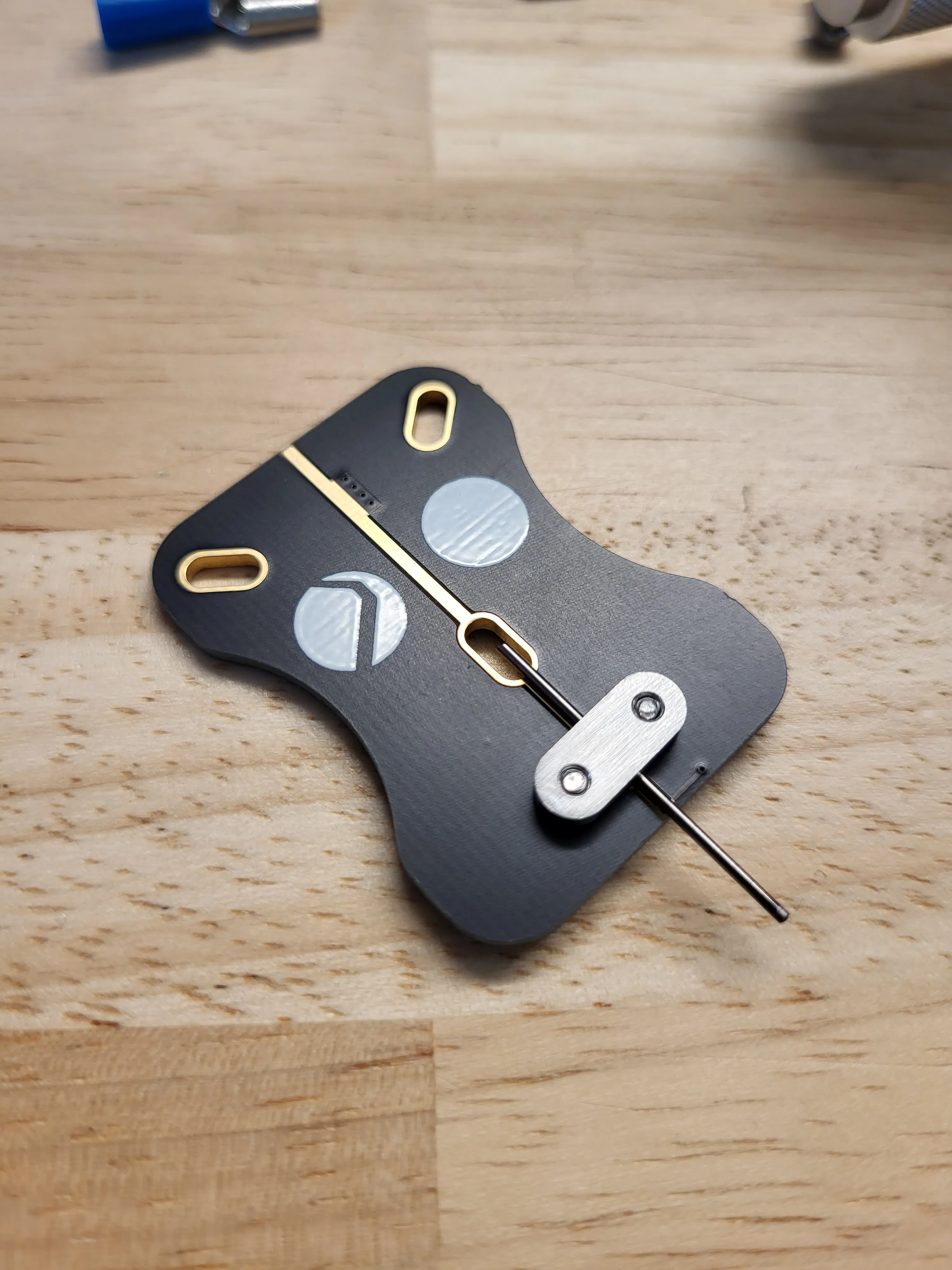 Black circuit board sample holder with gold-plated slots, a metal clamp and an electrode wire, on a wooden table