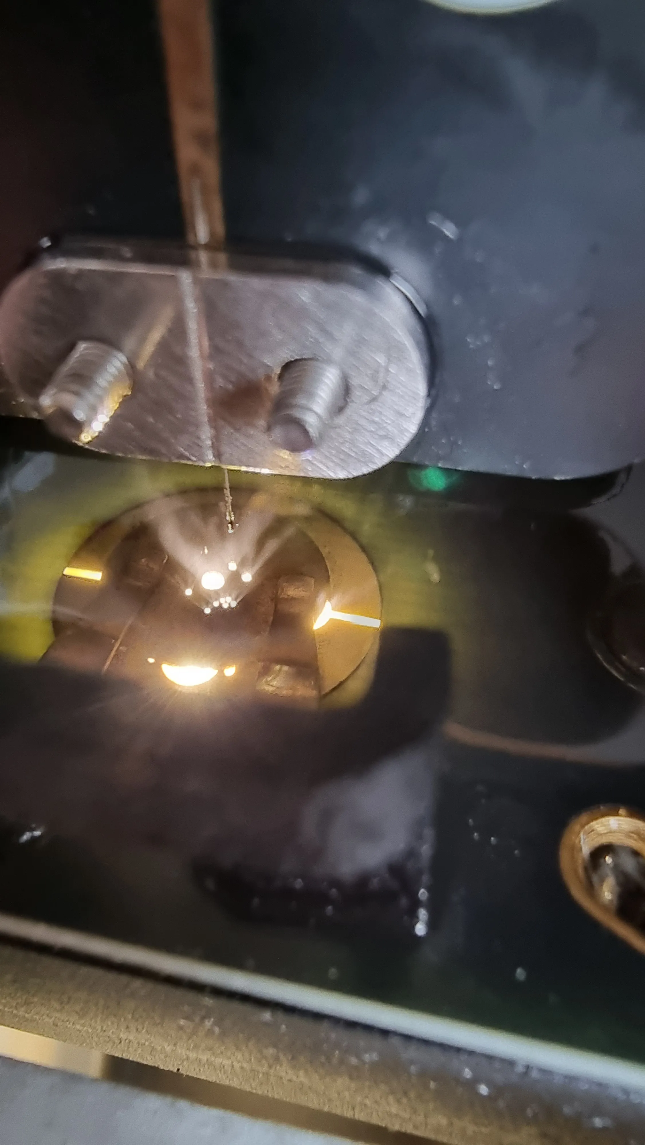 EDM drilling in progress inside the uDrill Pro: bright sparks at the tip of the electrode wire, under the metal clamp