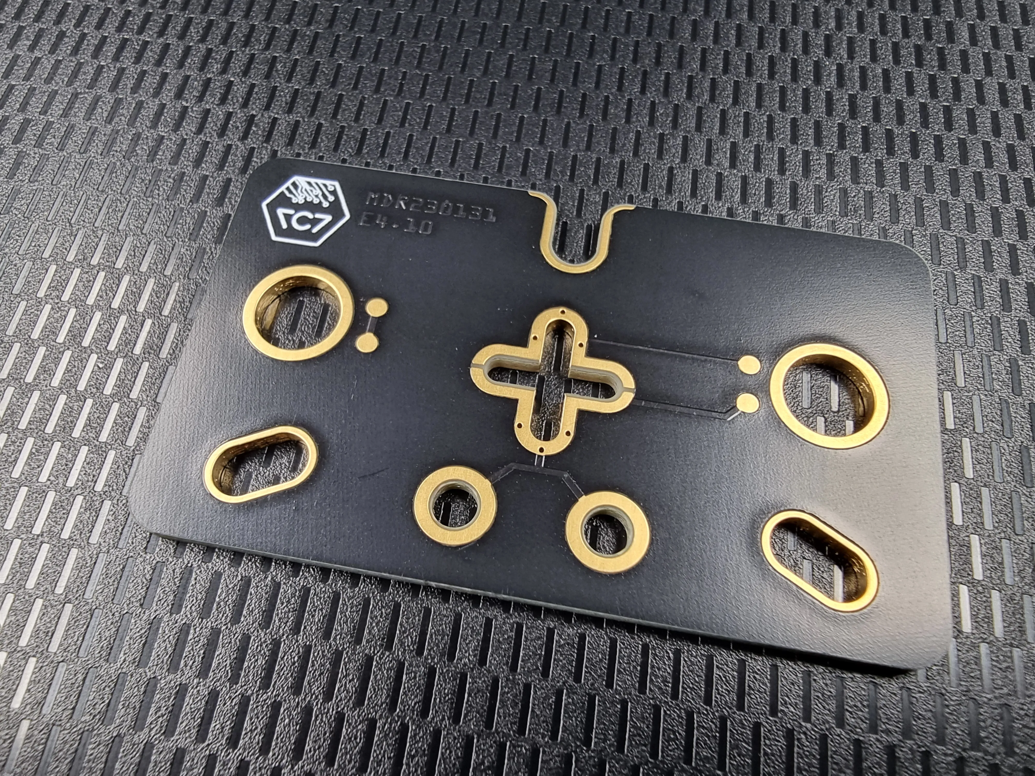 Black circuit board with gold-plated slots and openings and the 7c7 logo, on a textured surface
