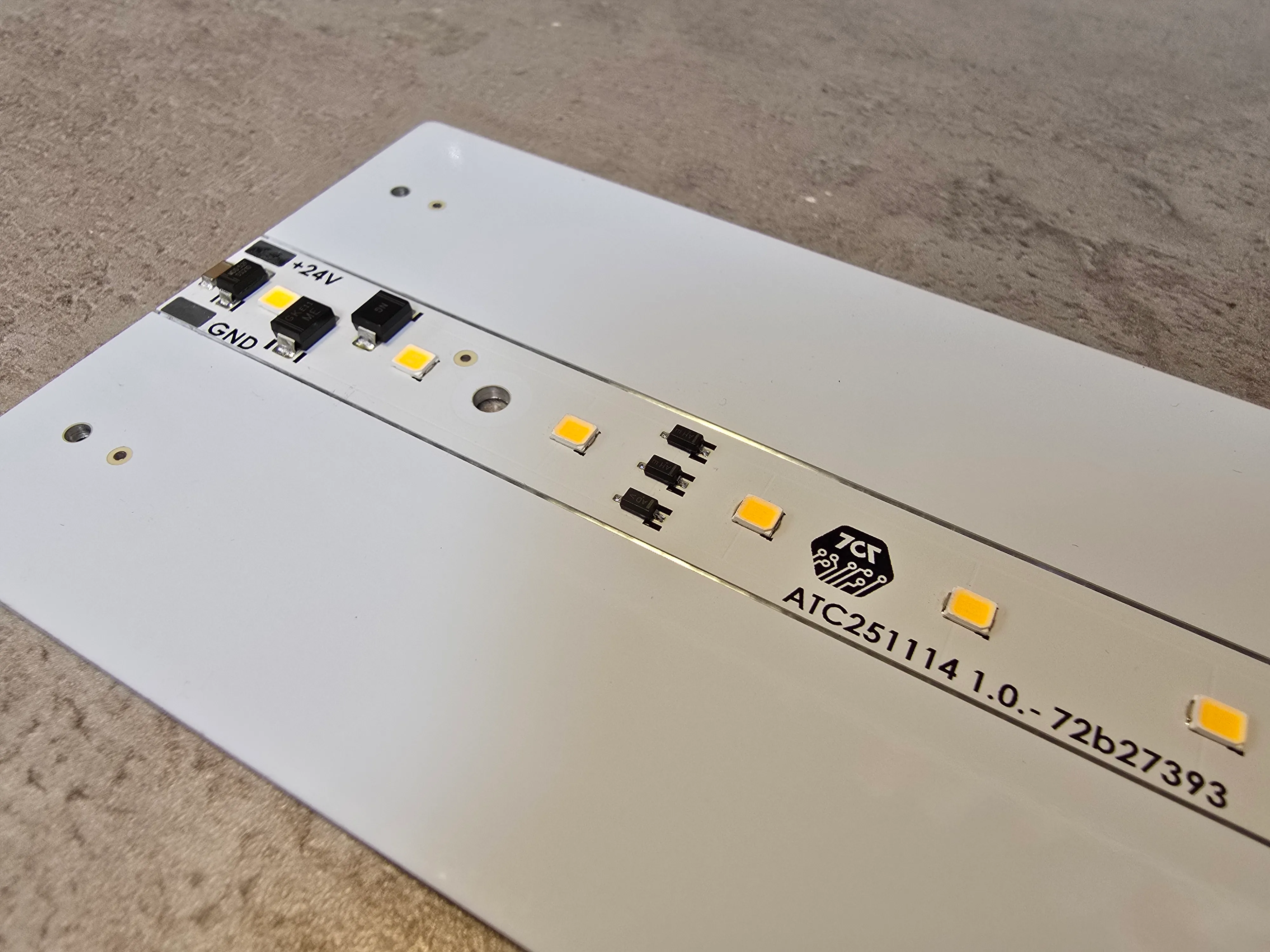 White LED strip circuit board with warm white LEDs, protection components, +24V and GND connections and the 7c7 logo